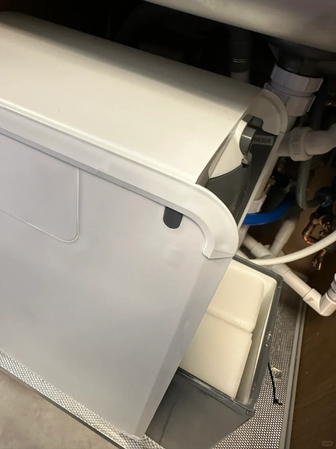 A white compact water softener unit installed under a sink cabinet, with its salt compartment pulled open to reveal salt blocks.