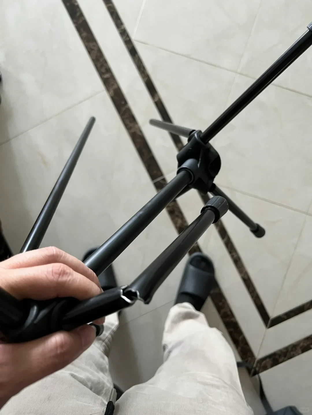 A person holds the broken leg of a black metal tripod or light stand, showing where the hollow metal tube has snapped in half.