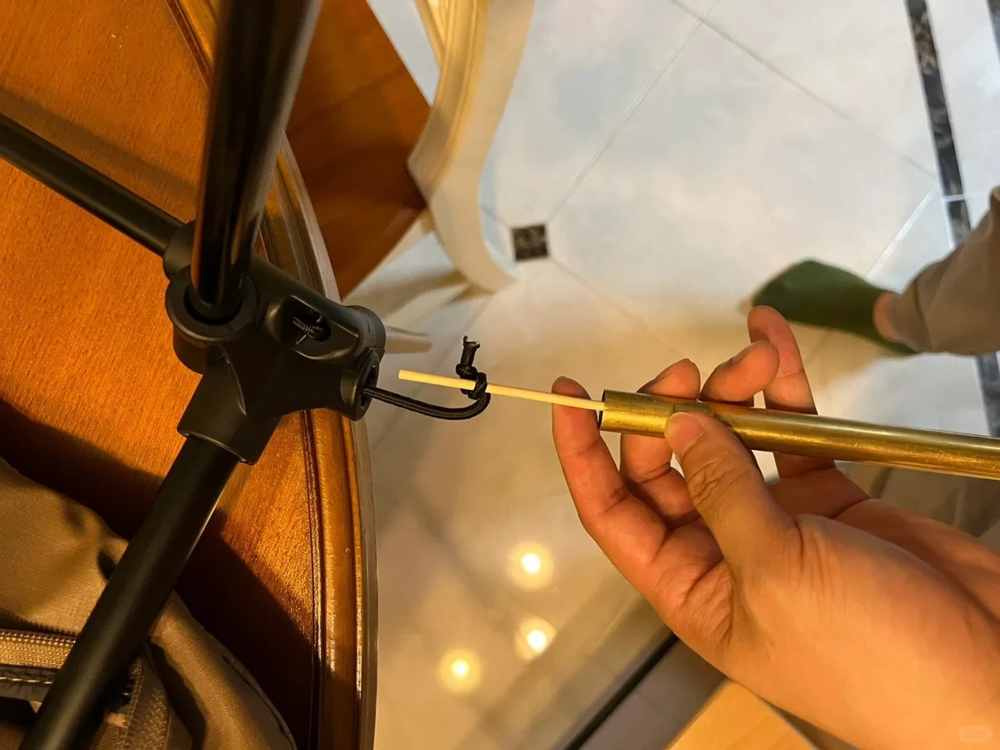 A person's hands holding a brass-toned tube of a folding frame, using a small wooden stick to secure the internal elastic cord pulled from a black plastic joint connector.