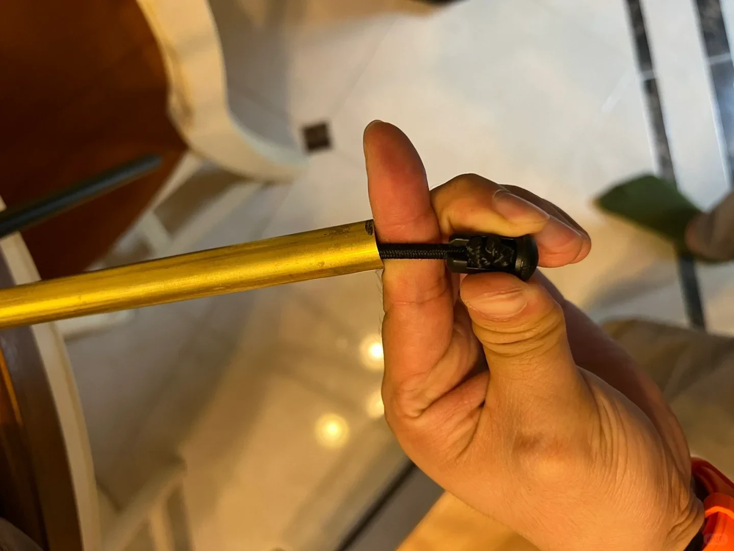 A person holding the end of a hollow gold metal tent pole while pulling out an internal elastic shock cord fitted with a black plastic end piece.