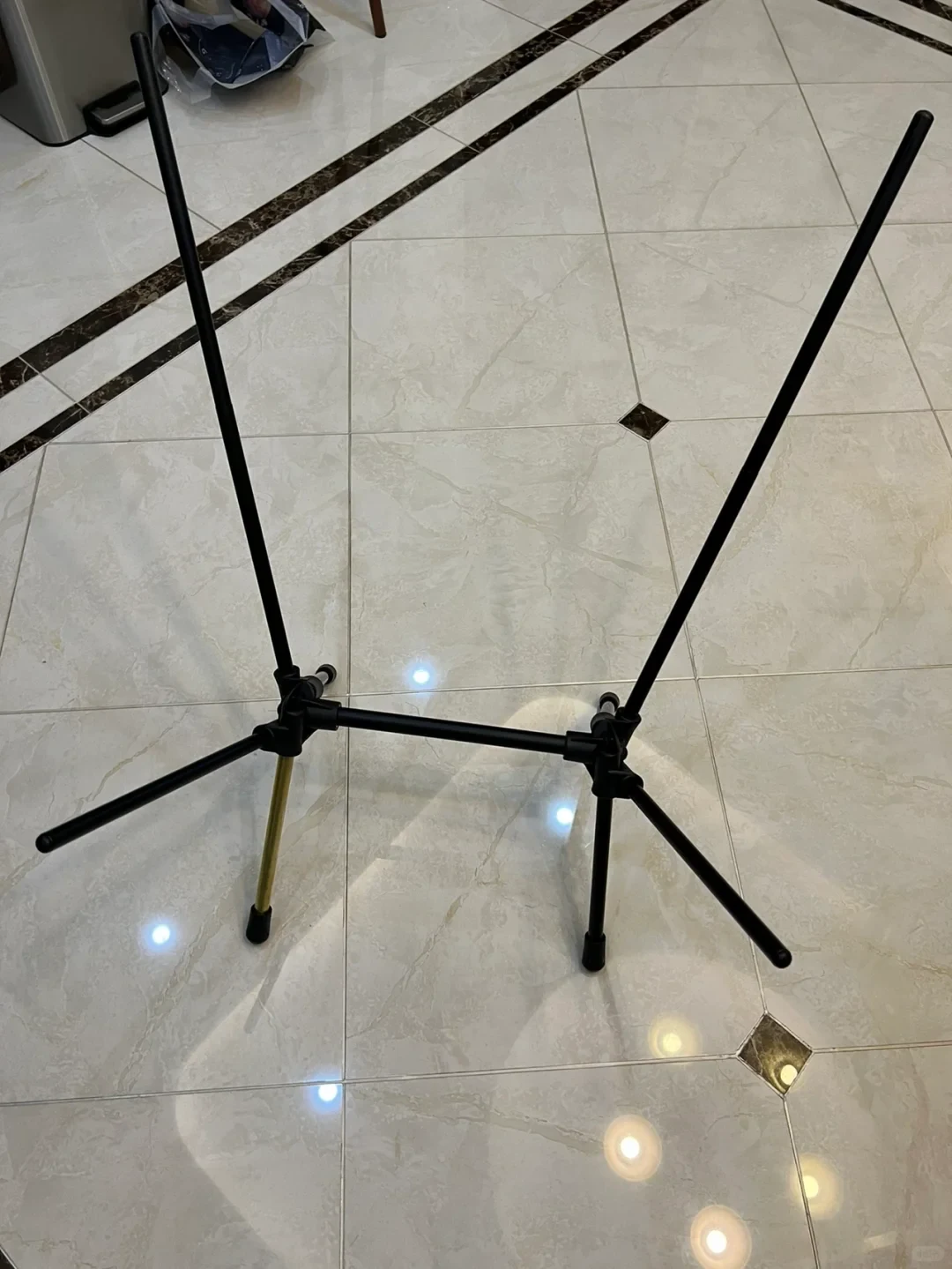 An assembled metal frame for a portable camping chair, mostly black with one gold-colored leg, stands on a polished tile floor.