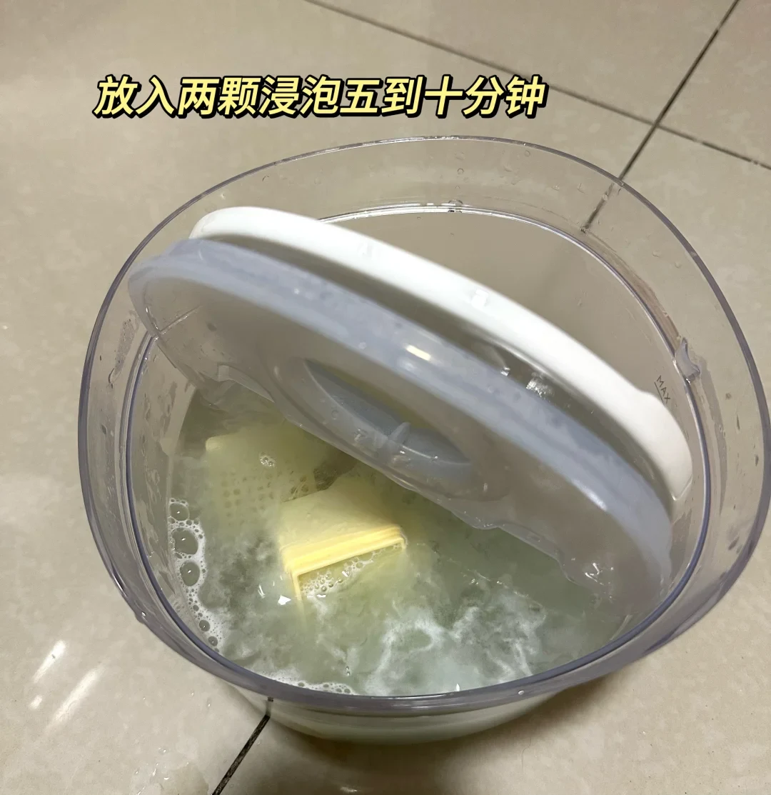 Clear round container filled with soapy water and submerged plastic parts under a tilted lid.