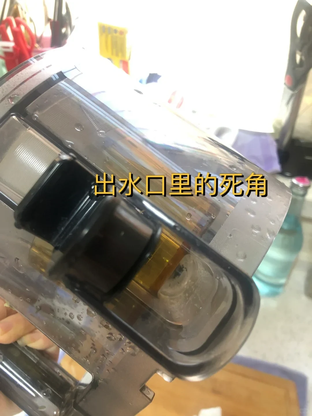 A hand holds the clear Hurom juicer chamber, showing the juice outlet and water droplets; the Chinese overlay points out a hard-to-reach corner inside the outlet.