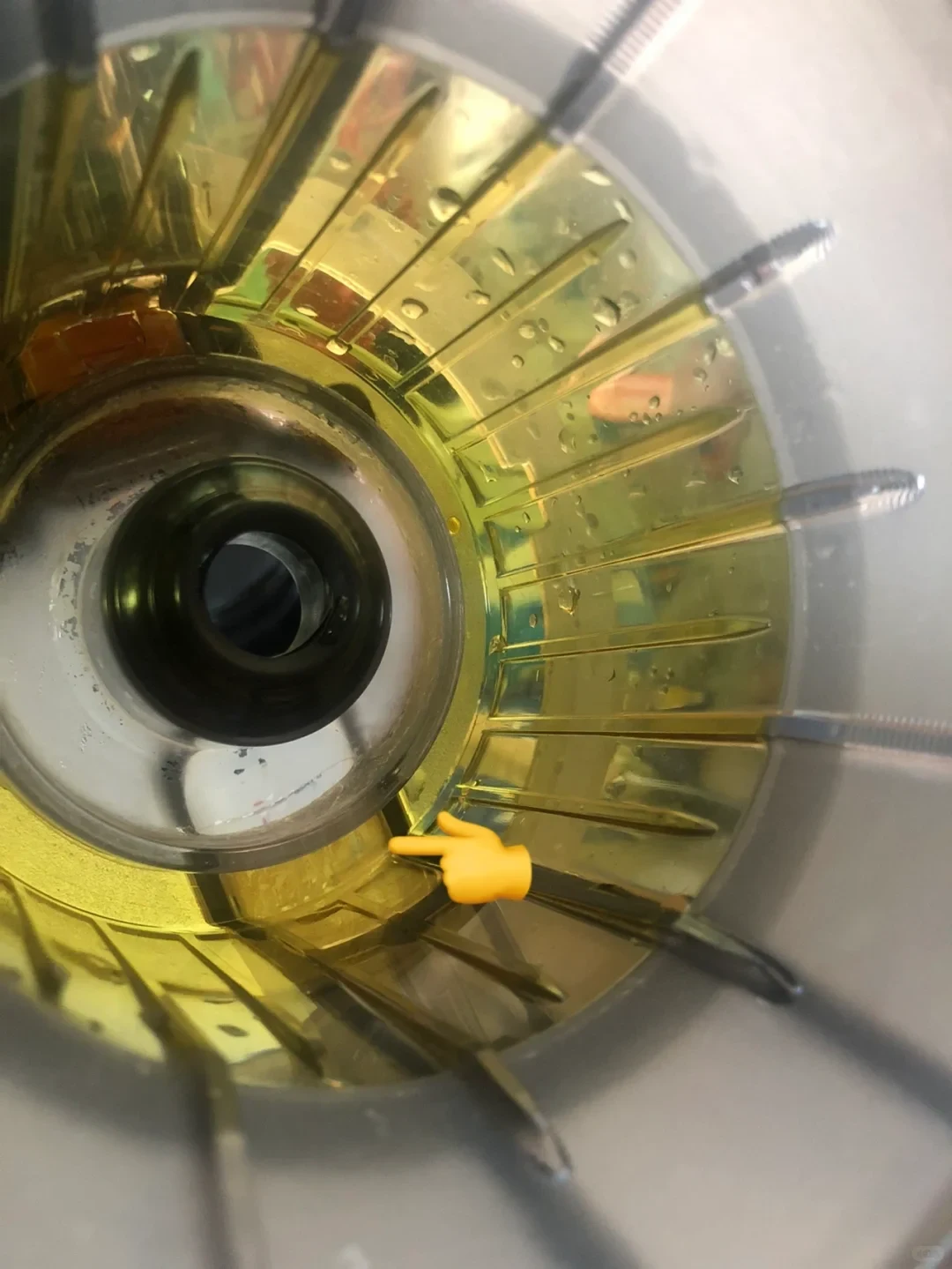 Close-up of a yellow-tinted transparent circular component with radial compartments and a central opening; a pointing-hand graphic indicates a small section near the lower edge.