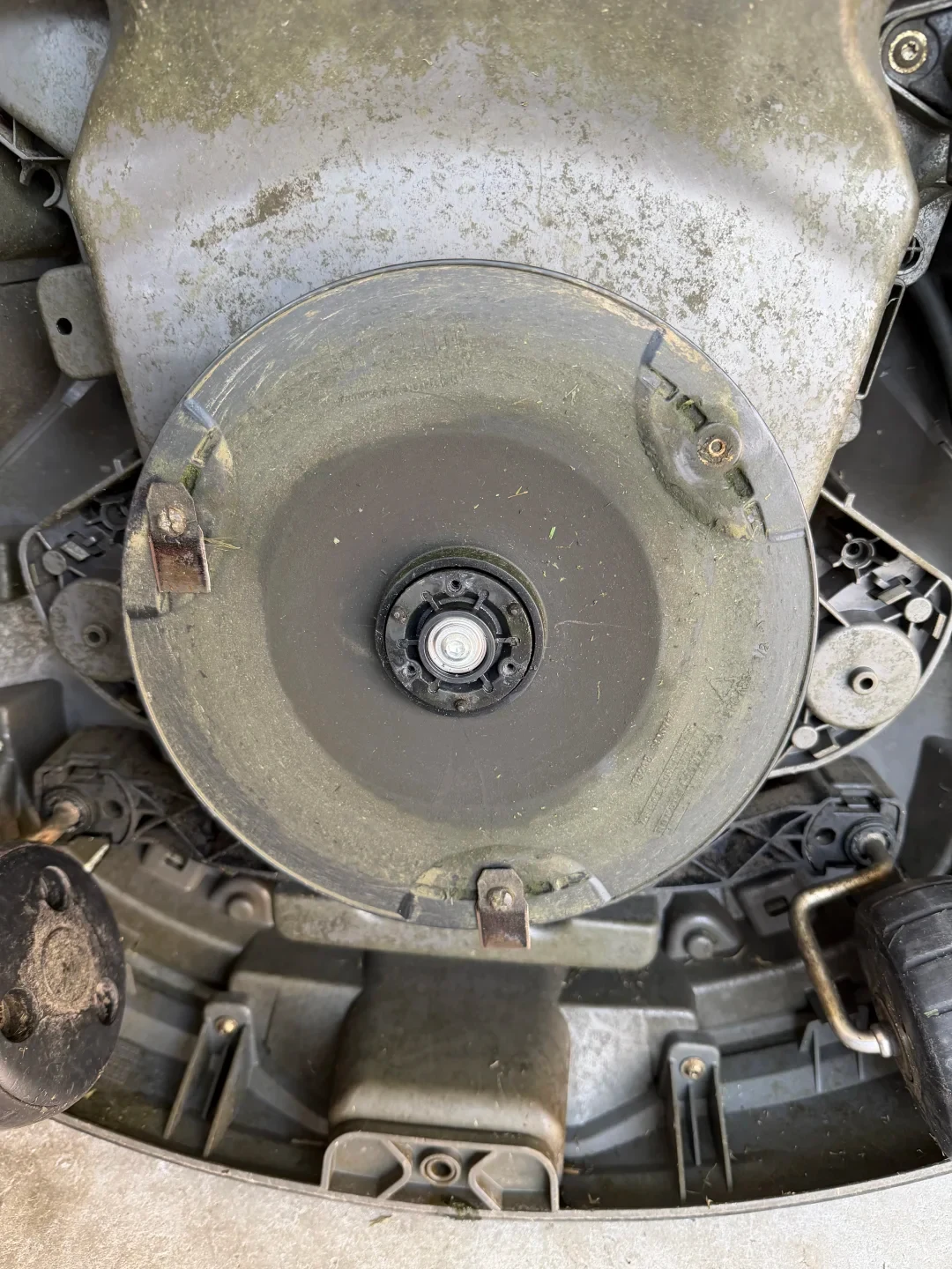 Underside view of a robotic lawn mower showing the circular cutting blade disc with small pivoting razor blades attached along its perimeter, the central mounting nut, wheels, and molded plastic chassis.