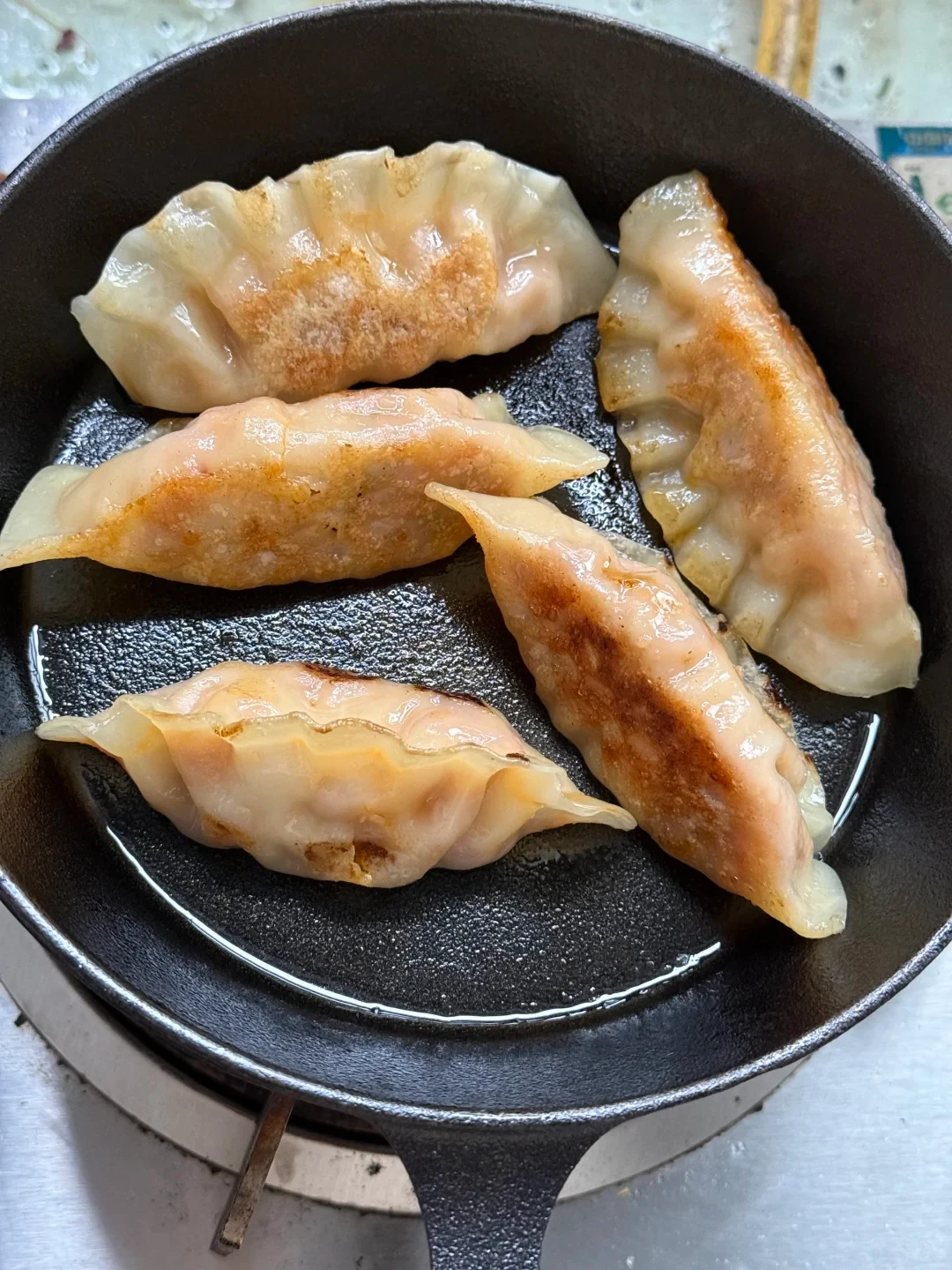 Five golden-brown pan-fried dumplings cooking in oil inside a black cast iron skillet.