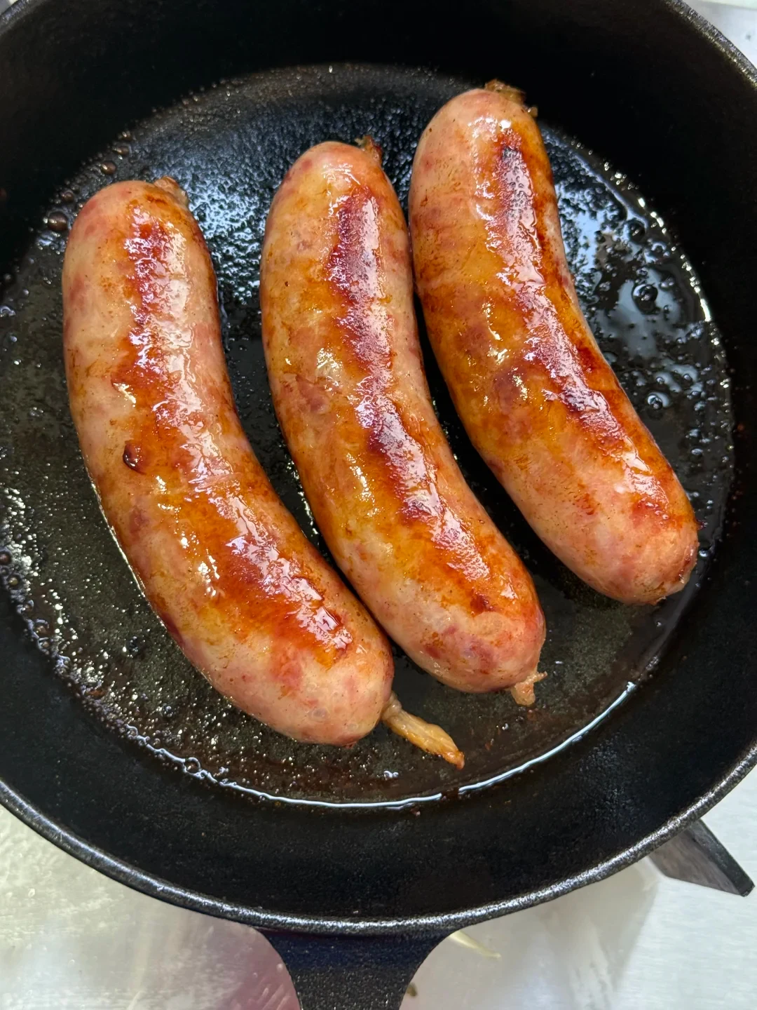 Three plump sausages frying to a golden-brown finish in a black cast iron skillet.