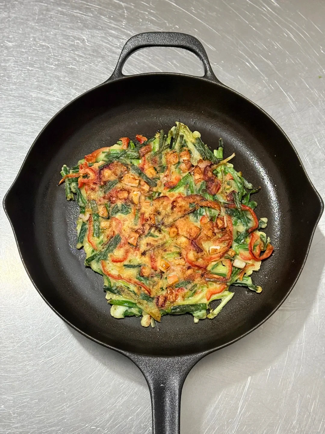 A round vegetable pancake in a black cast-iron skillet with a long handle and helper loop.