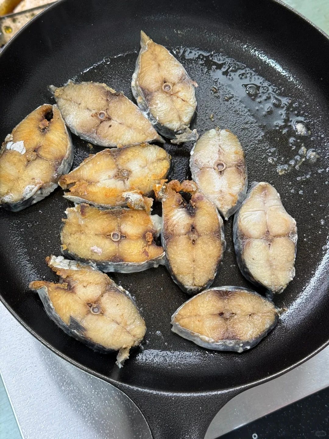 Multiple cut fish steaks pan-frying in oil inside a black skillet.