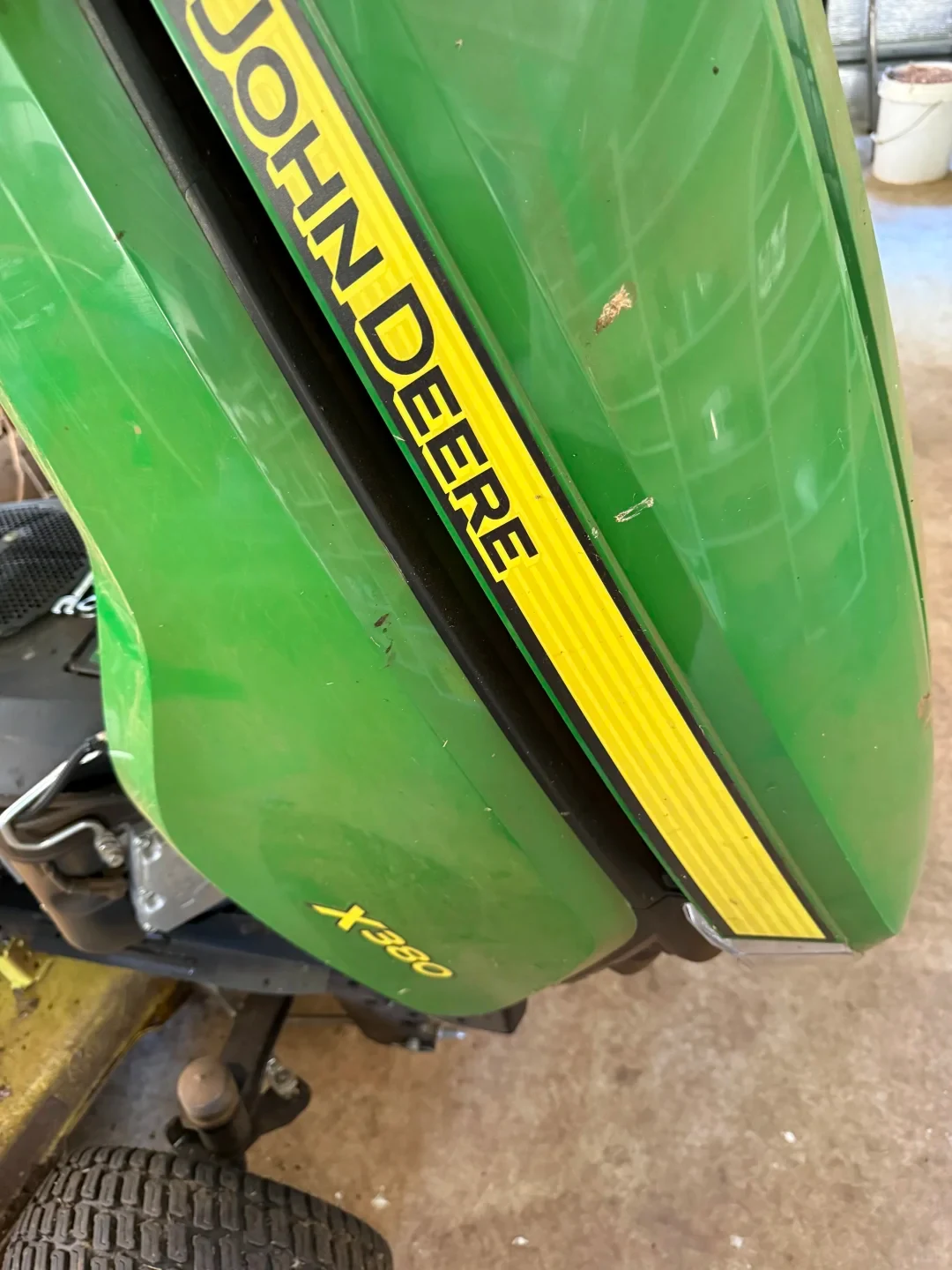 Close-up view of the green hood of a John Deere X380 lawn tractor featuring the yellow branded stripe and model lettering above the front wheel.