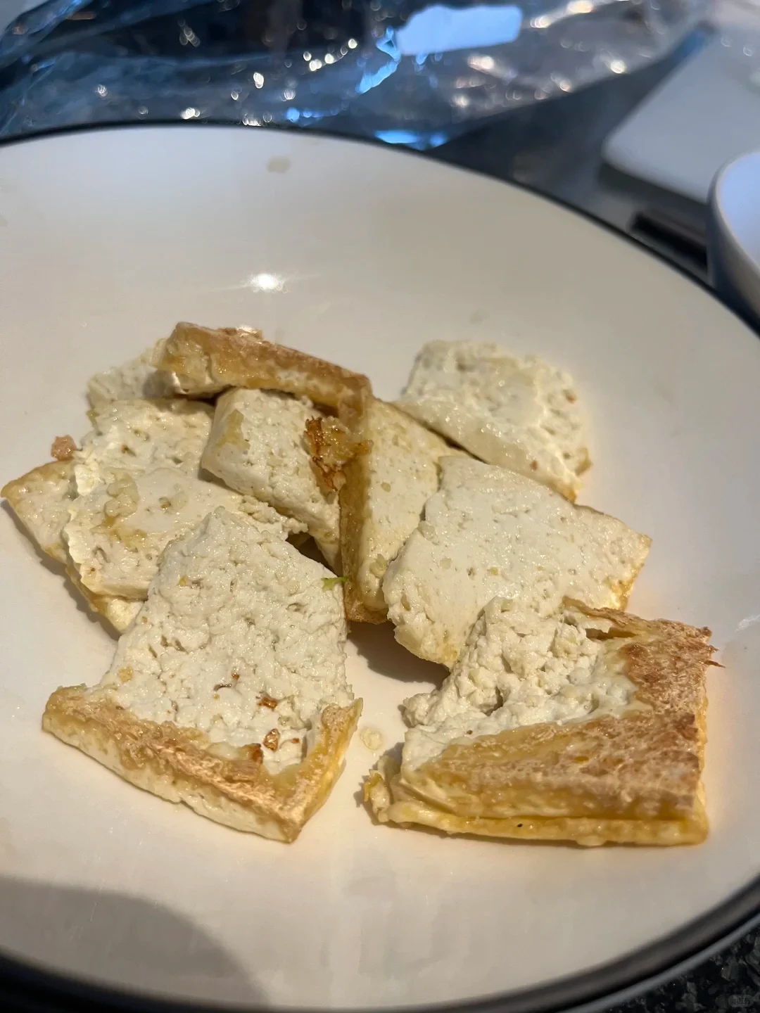 Pieces of pan-fried tofu with crispy golden-brown edges served in a white bowl.