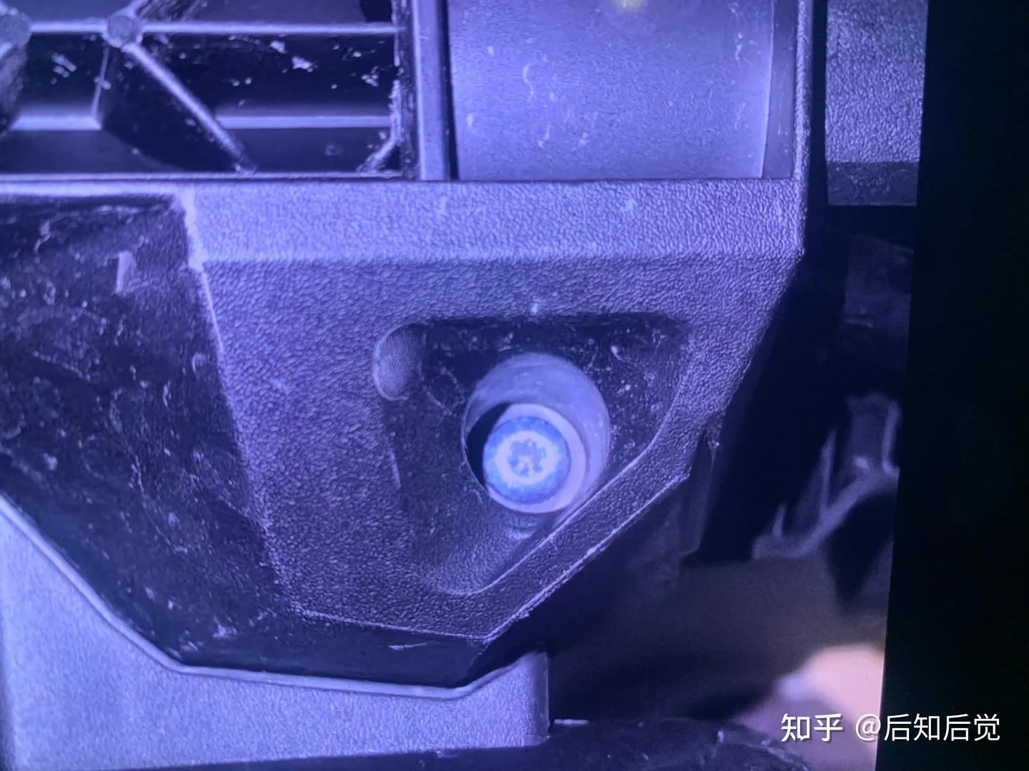 Close-up of a white circular fitting or fastener mounted in the dark textured housing of a disassembled pressure washer.