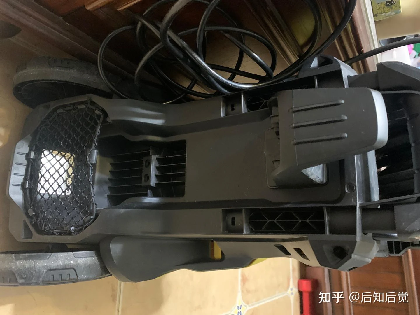 A dark gray pressure washer lies on its side with its housing and internal openings exposed, surrounded by coiled cables and loose parts.
