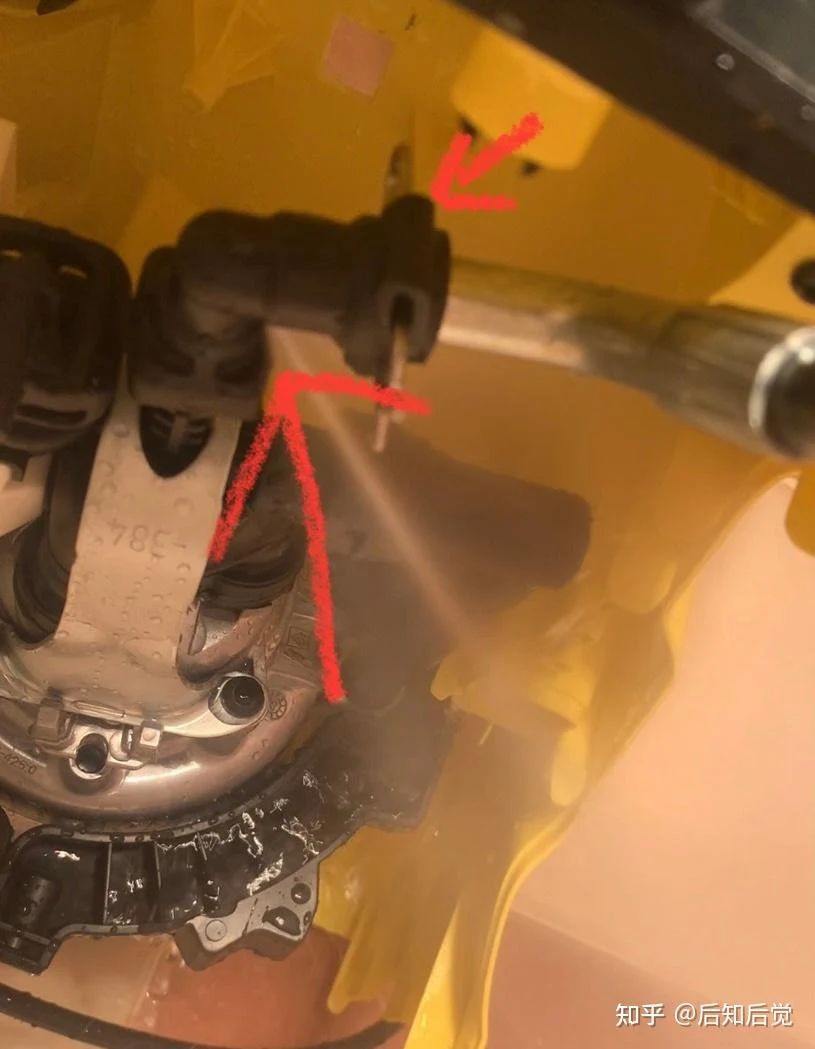 Close-up of a disassembled Kärcher K3dp pressure washer showing the pump assembly and a black plastic outlet fitting inside the yellow housing, with red arrows pointing to the fitting.