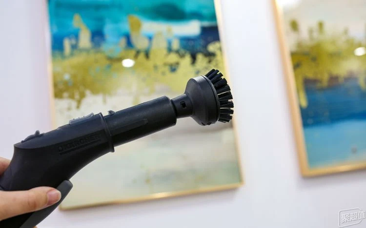 A hand holding the black steam cleaner handle fitted with the small round brush attachment.