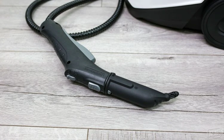 A close-up view of the ergonomic steam handle and detail nozzle attachment connected by a flexible hose to the Kärcher SC3 steam cleaner on a light wood floor.