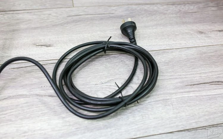 Coiled black power cord with a three-prong plug resting on a light wood-grain floor.