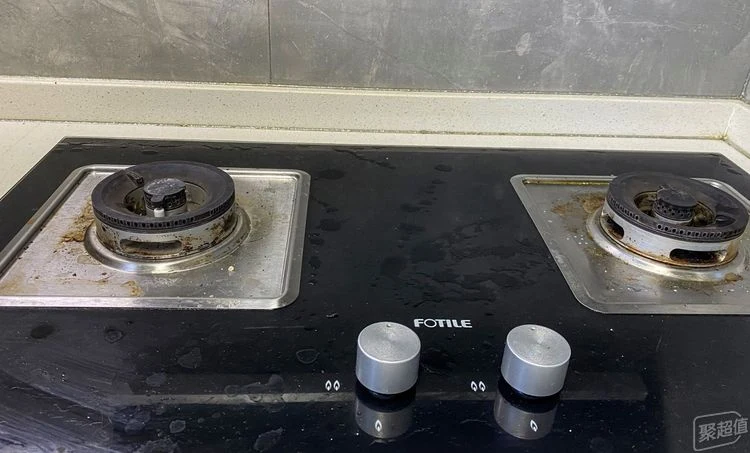 A dirty black glass Fotile gas stovetop showing accumulated grease and burnt-on grime around the dual burners before cleaning.