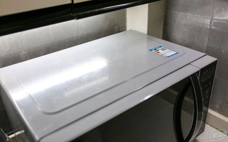 High-angle view of the top and front panel of a silver-gray microwave oven on a kitchen counter under under-cabinet lighting.