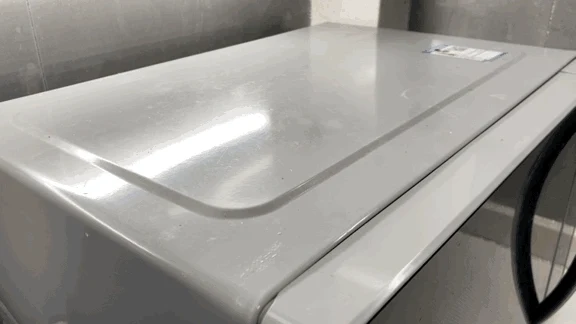 Top surface of a white kitchen appliance resting against a wall before steam cleaning.