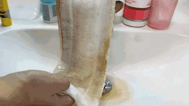 A person holding the microfiber mop pad over a white sink as water rinses away dirt and stains.