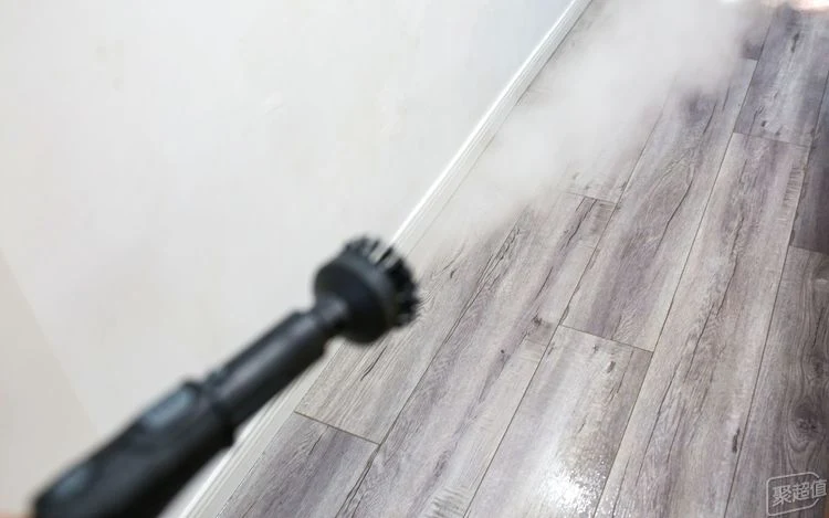 Kärcher steam cleaner nozzle fitted with a small round brush spraying a plume of white steam across wood-plank flooring.