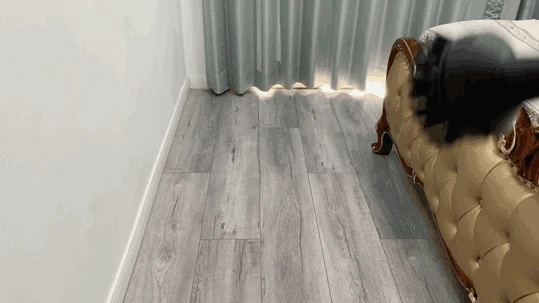 A user maneuvers the swiveling floor nozzle of a Kärcher steam cleaner along the wood-grain laminate flooring between a wall and a bed.
