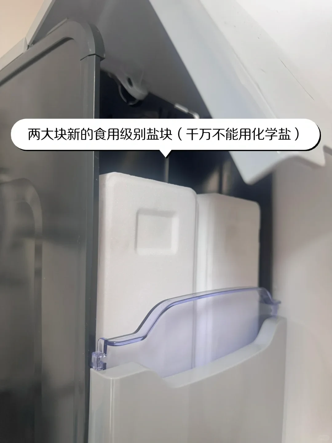Two large rectangular white salt blocks set inside an open appliance compartment behind a plastic guard.
