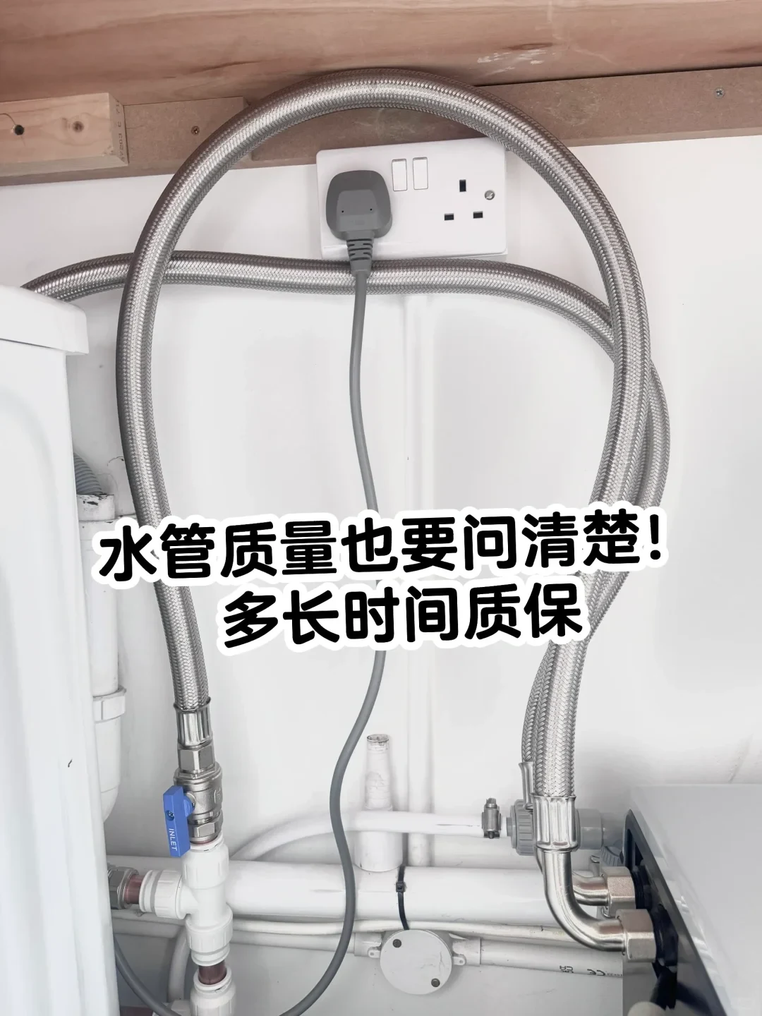 Plumbing setup with looped braided stainless steel water hoses connected to valves and PVC pipes under a counter near a UK wall power socket.