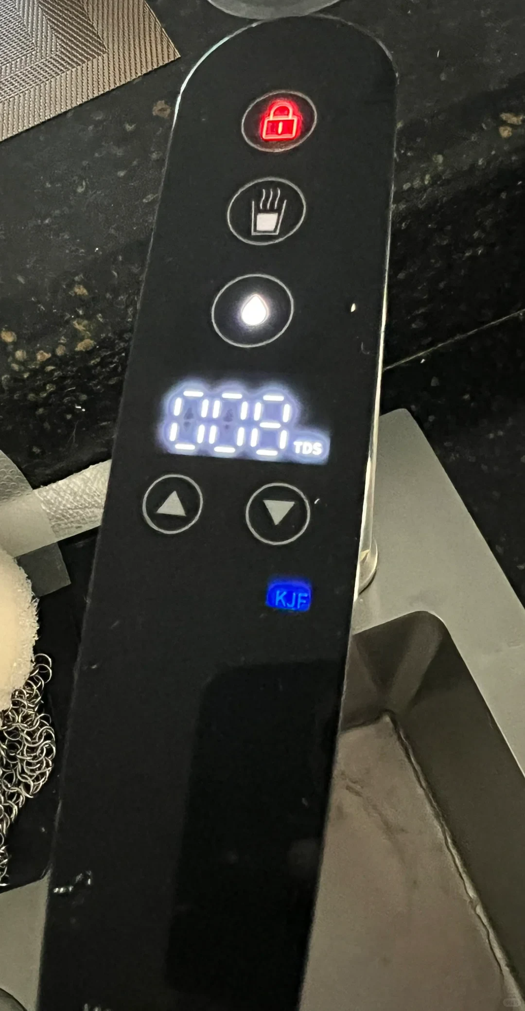 A close-up of a black smart water dispenser faucet touch panel featuring illuminated icons including a red child lock, a cup with steam, a water droplet, a digital display reading 008 TDS, directional adjustment arrows, and a blue KJF indicator.