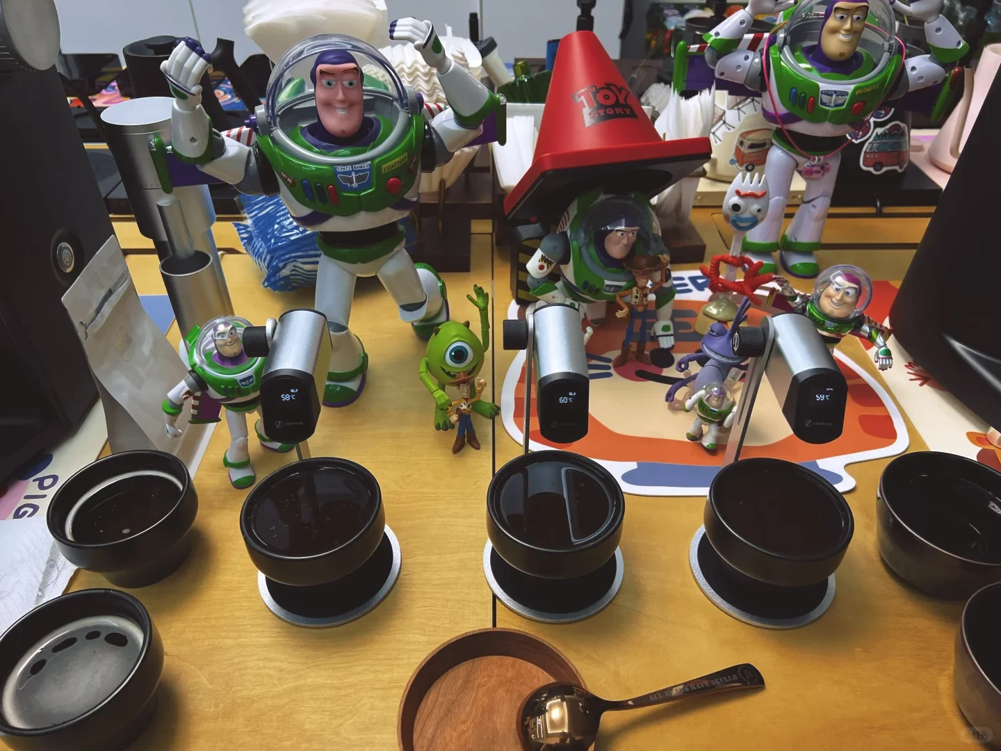 Black cupping bowls and stacked cups are arranged with probe thermometers, wooden dishes and a spoon, with decorative figures behind them.