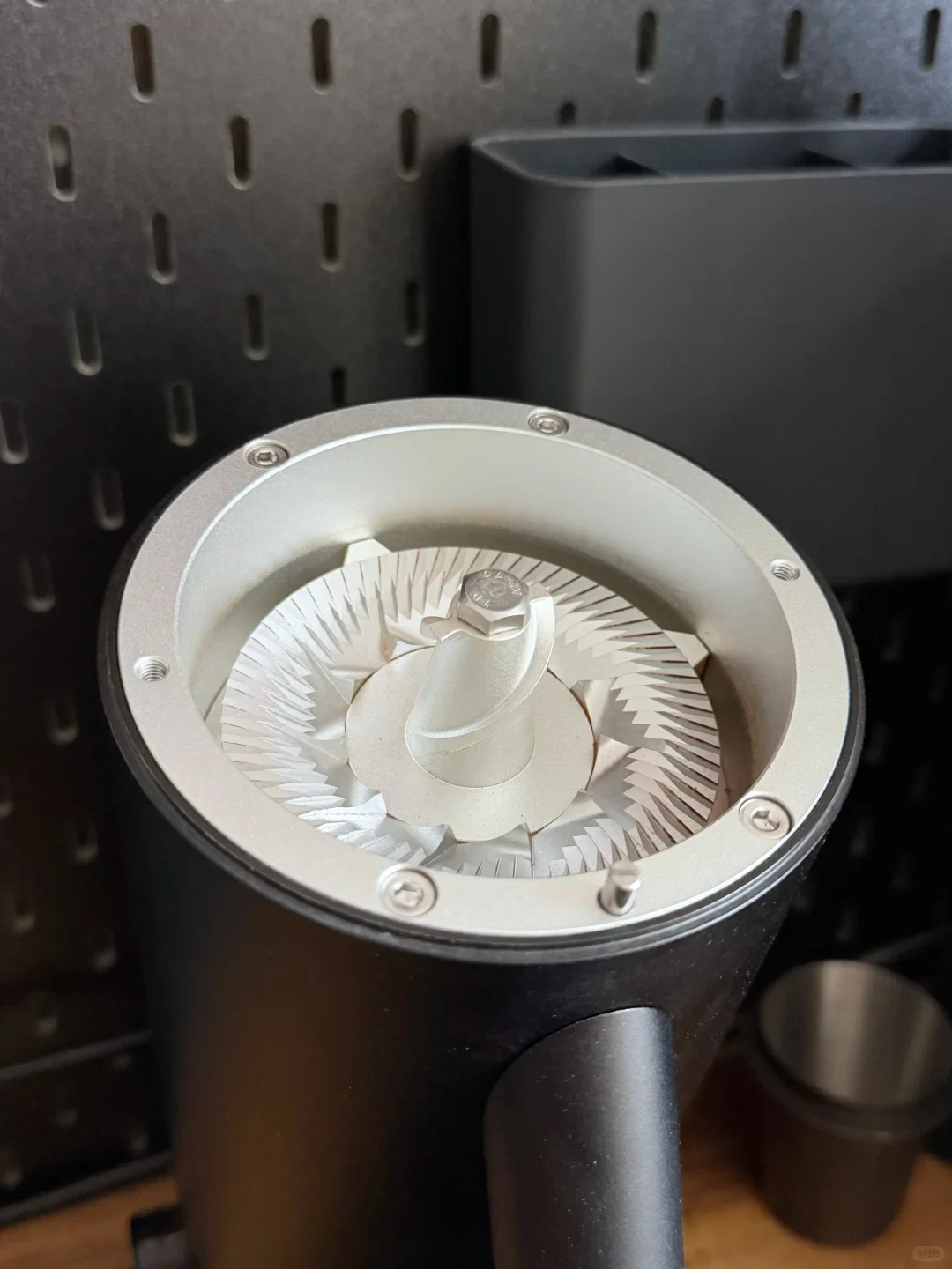 An opened black LAGOM P80 electric coffee grinder shows its silver flat burr and central auger, with a perforated metal panel behind it.