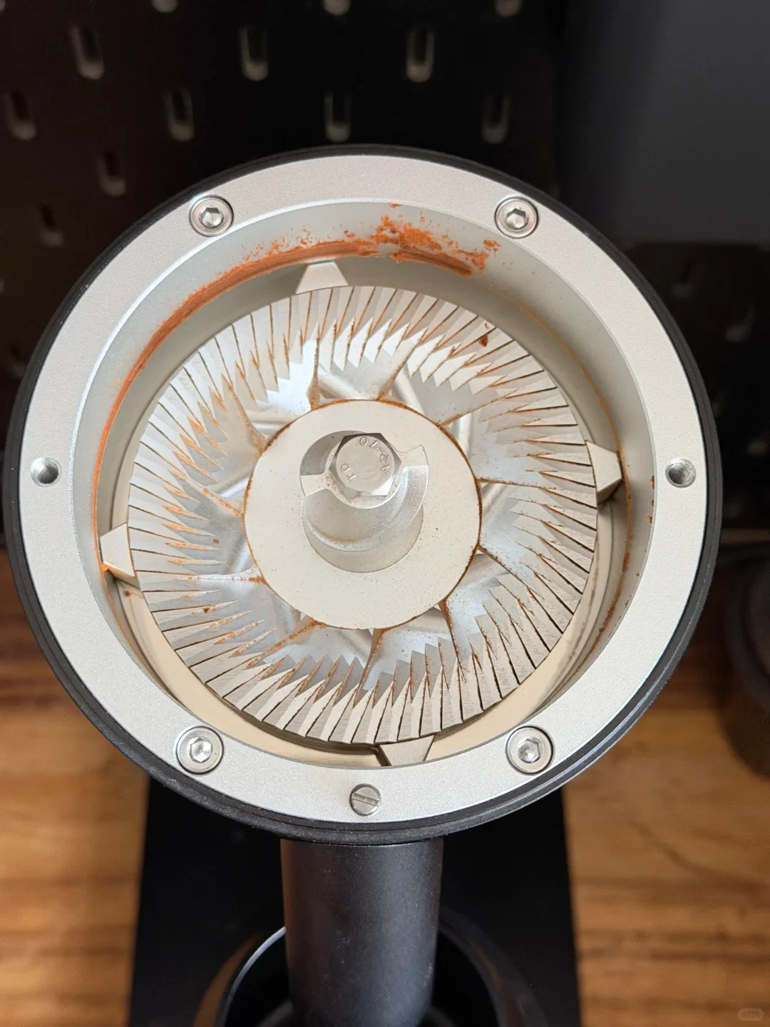 Close-up of an opened coffee grinder showing its circular burr assembly, with orange-brown coffee residue around the inner rim and on the burrs.