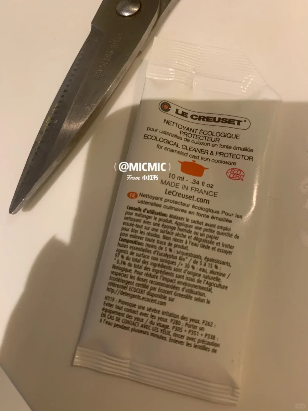 A sample sachet of Le Creuset Ecological Cleaner and Protector for enameled cast iron cookware resting next to the blade of stainless steel scissors.