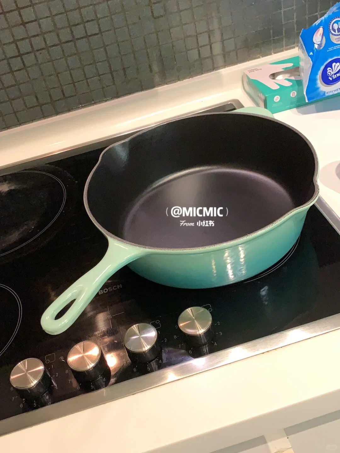 A mint green enameled cast iron skillet with a black interior sitting on a black Bosch stovetop.