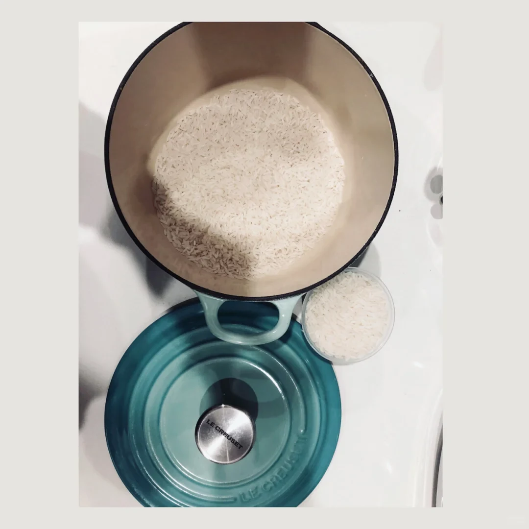 Overhead photo of an open teal enameled pot containing uncooked rice, with its matching lid below and a small clear cup of rice beside it.