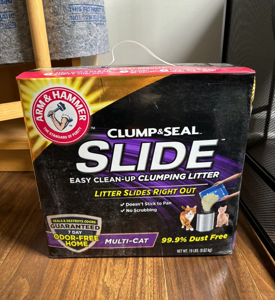 A 19-pound box of Arm & Hammer Clump & Seal Slide clumping litter on a wooden floor.