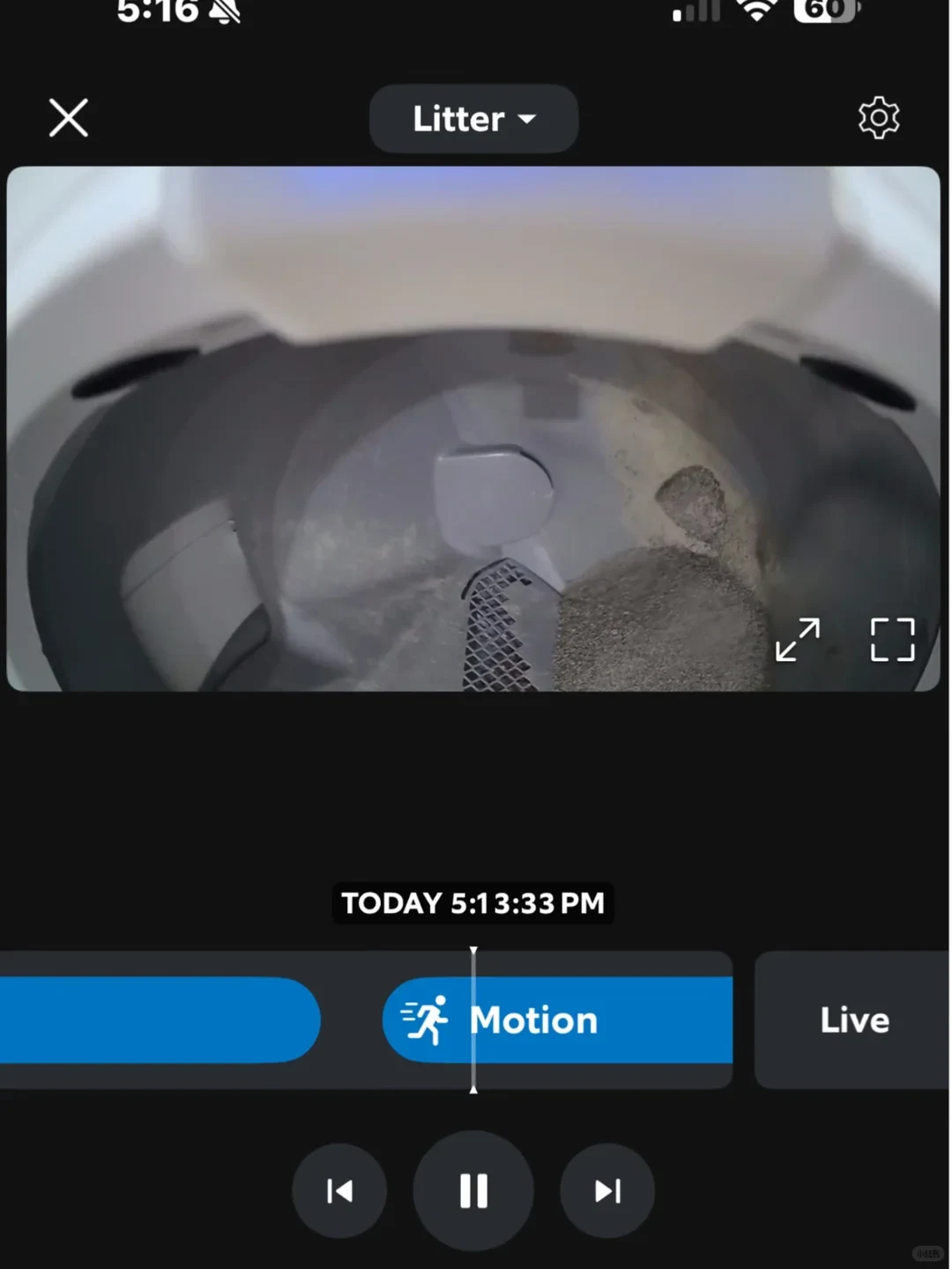 A smartphone interface displaying a live internal camera feed of an automatic cat litter box filled with litter. Below the video player is a timeline marker indicating 'Motion' detected at 5:13:33 PM, along with standard video playback controls.
