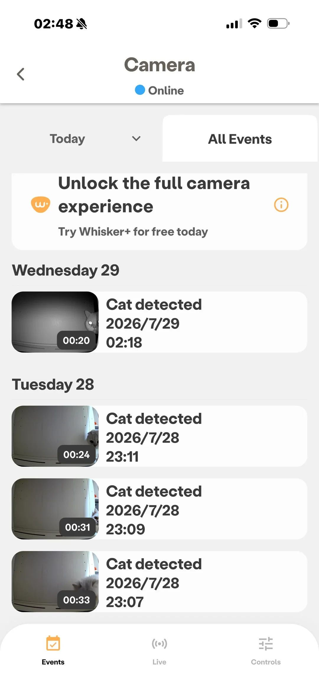 A smartphone app screen displaying camera event logs for a pet monitoring device. Under the heading 'Camera' marked as 'Online', tabs for 'Today' and 'All Events' appear above a banner promoting Whisker+. Below are timestamped video recording events labeled 'Cat detected' from Wednesday 29 and Tuesday 28, each with thumbnail previews showing a cat near an enclosed pet area, along with clip durations. Navigation tabs at the bottom include Events, Live, and Controls.