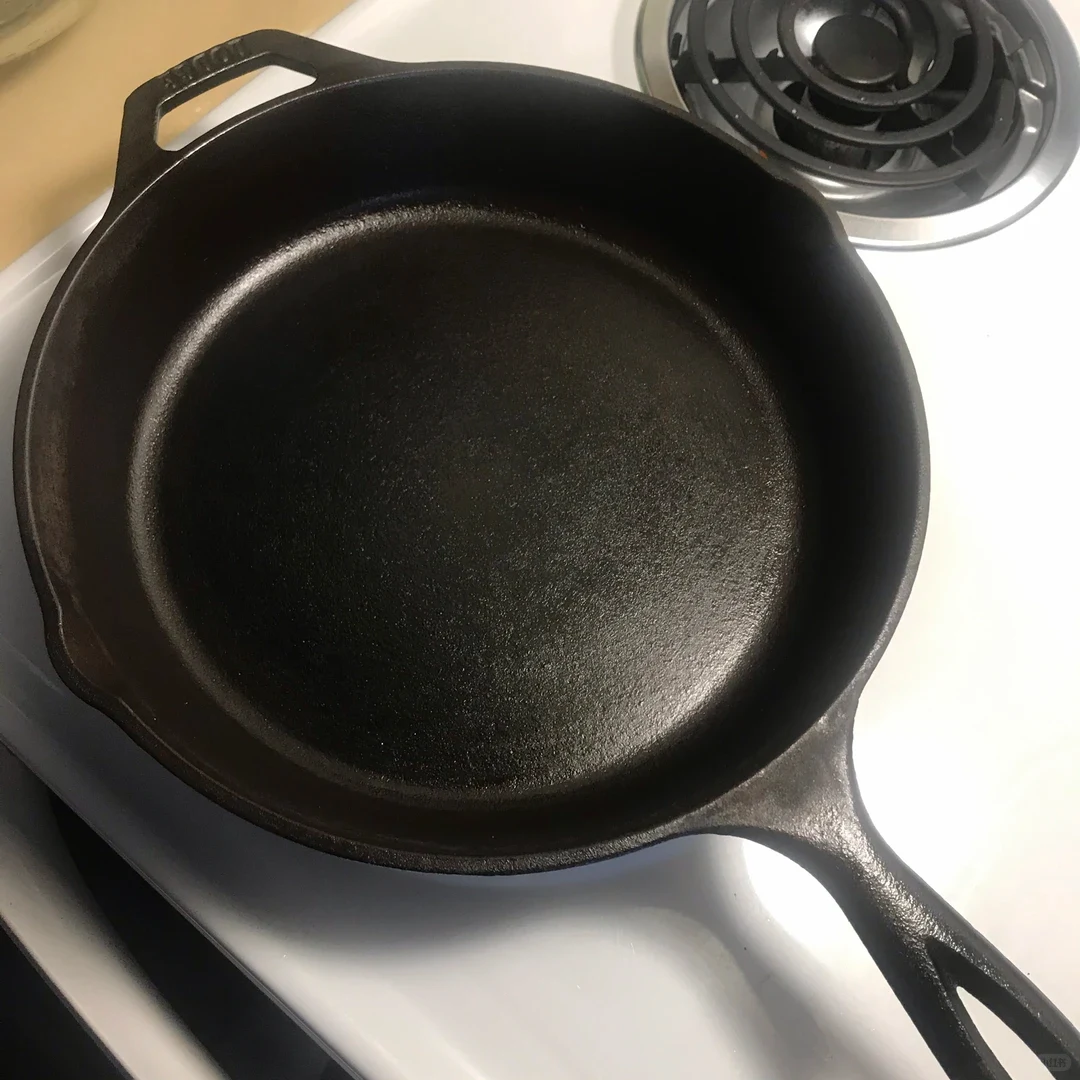 A seasoned black cast-iron skillet resting on a white electric coil stovetop.