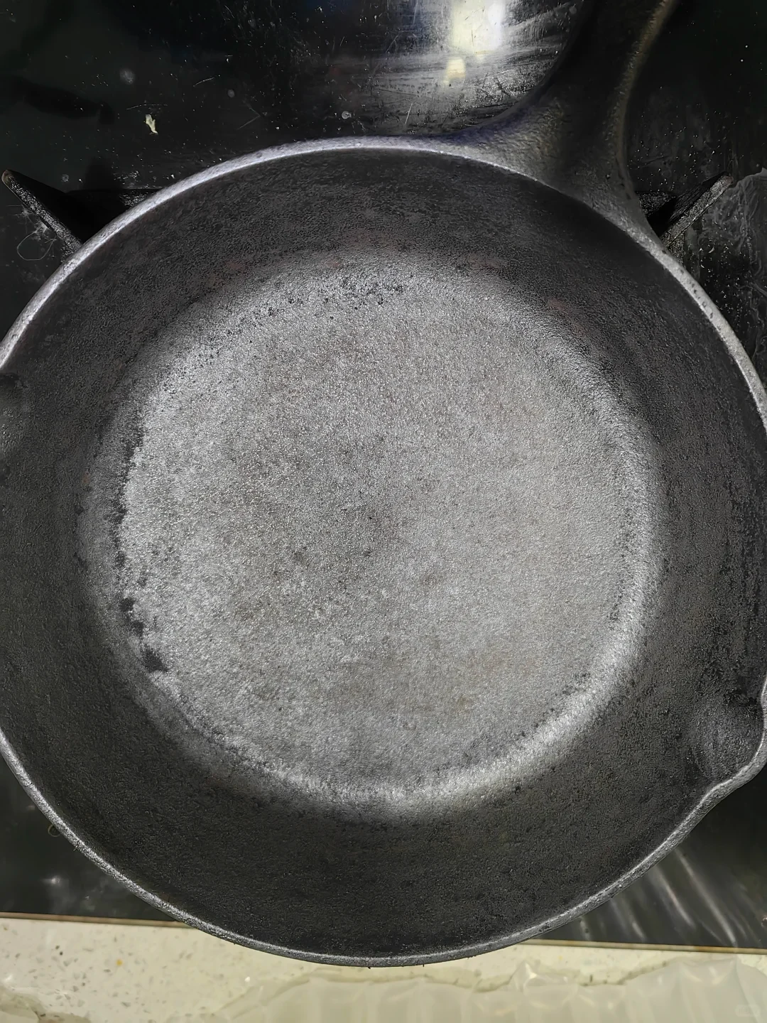 Overhead view of the cast-iron skillet after the owner’s cleanup, with a lighter cooking surface and a few dark patches remaining toward the sides.