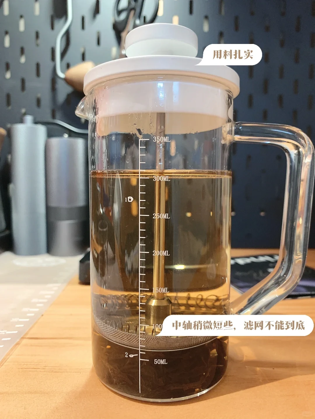 The owner’s Coffee Plus glass French press contains tea and tea leaves. Its filter stops above the bottom; Chinese labels describe sturdy construction and the shorter central shaft.