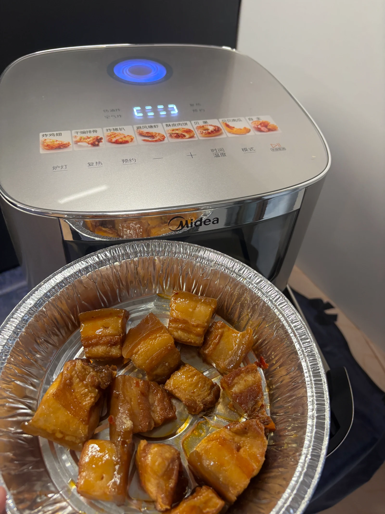 Browned pork pieces in a foil tray in front of the air fryer.