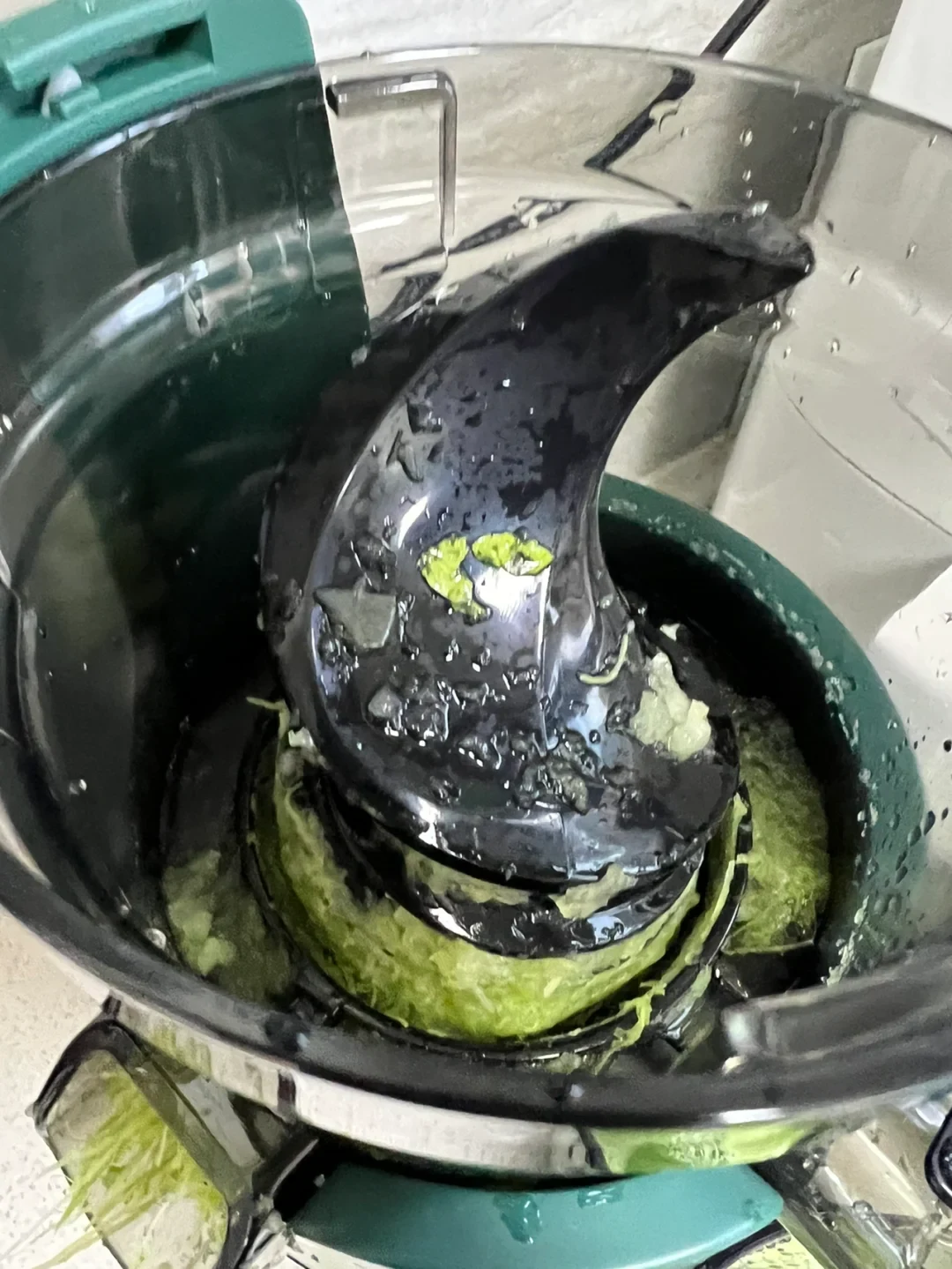 A green-and-black juicer contains leafy green pulp beneath its dark central pressing mechanism.