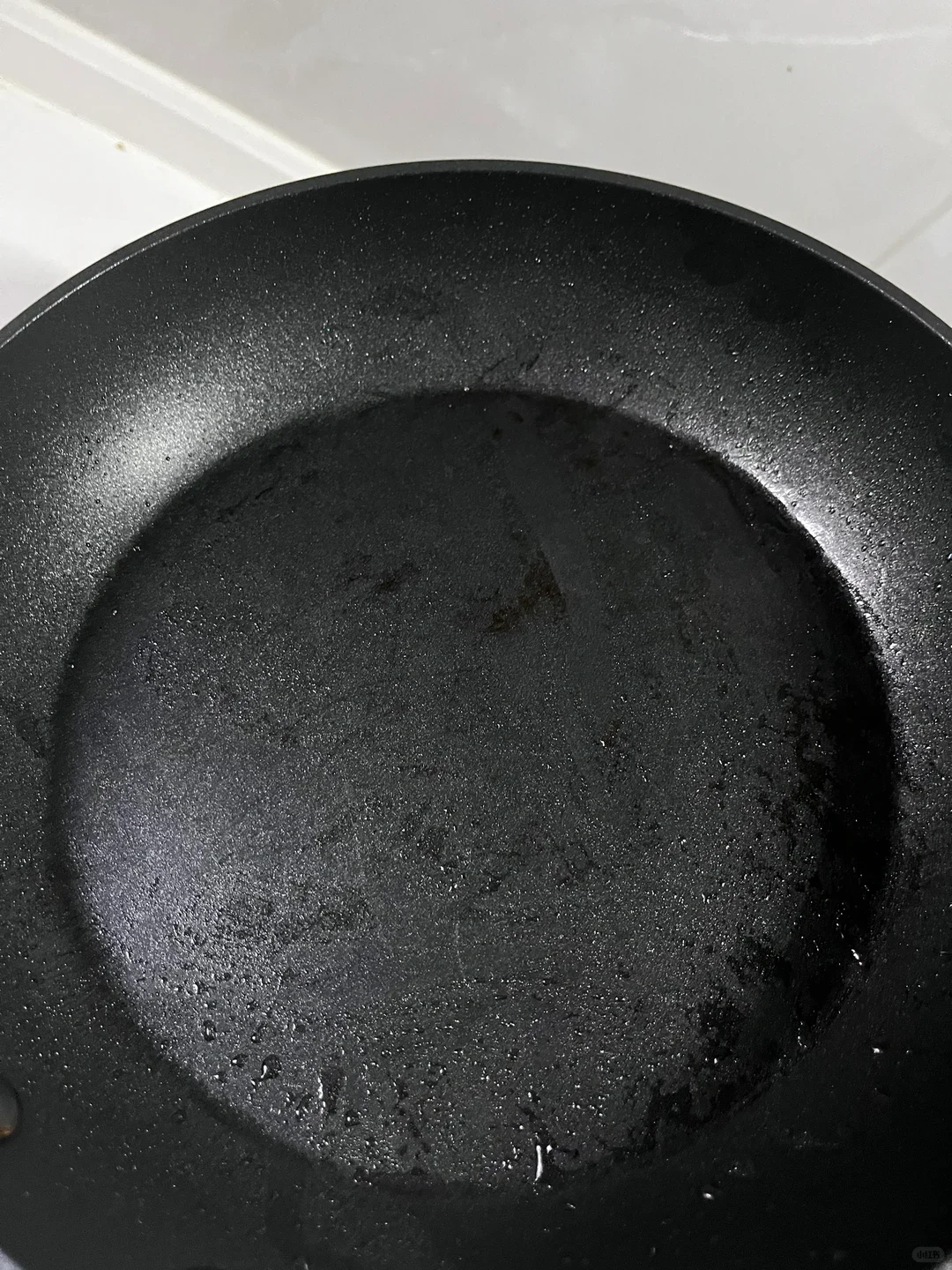 Top-down view of the dark, textured interior of a black frying pan showing light moisture and water droplets on the surface.