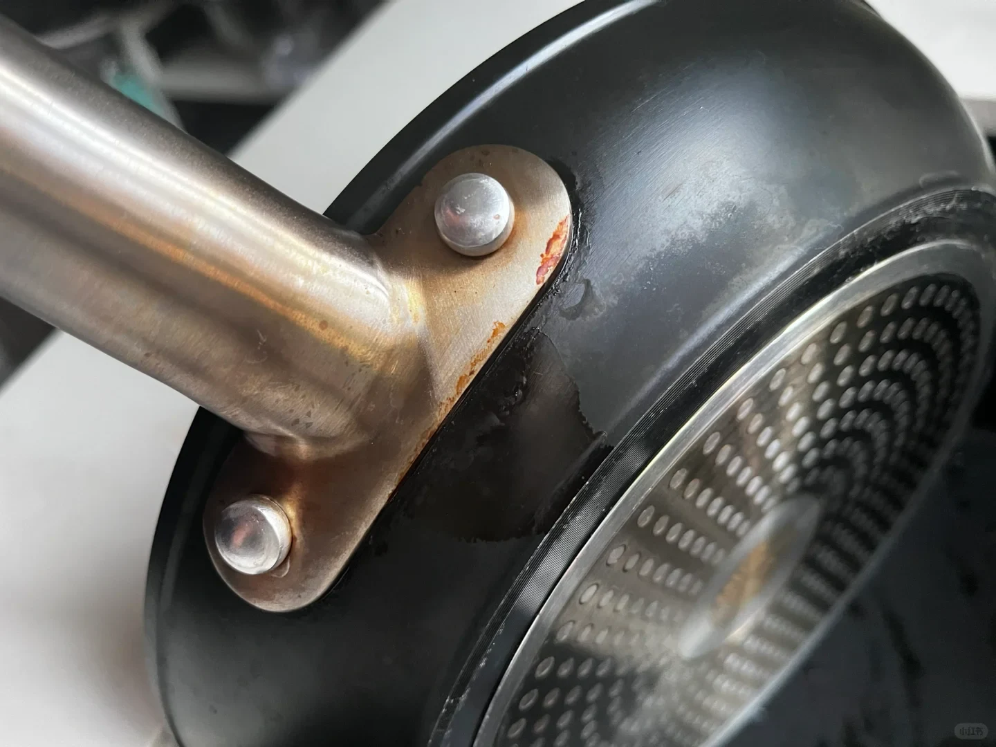 Close-up view of the exterior of a black frying pan, showing grease buildup and burnt residue around the base of the riveted stainless steel handle.