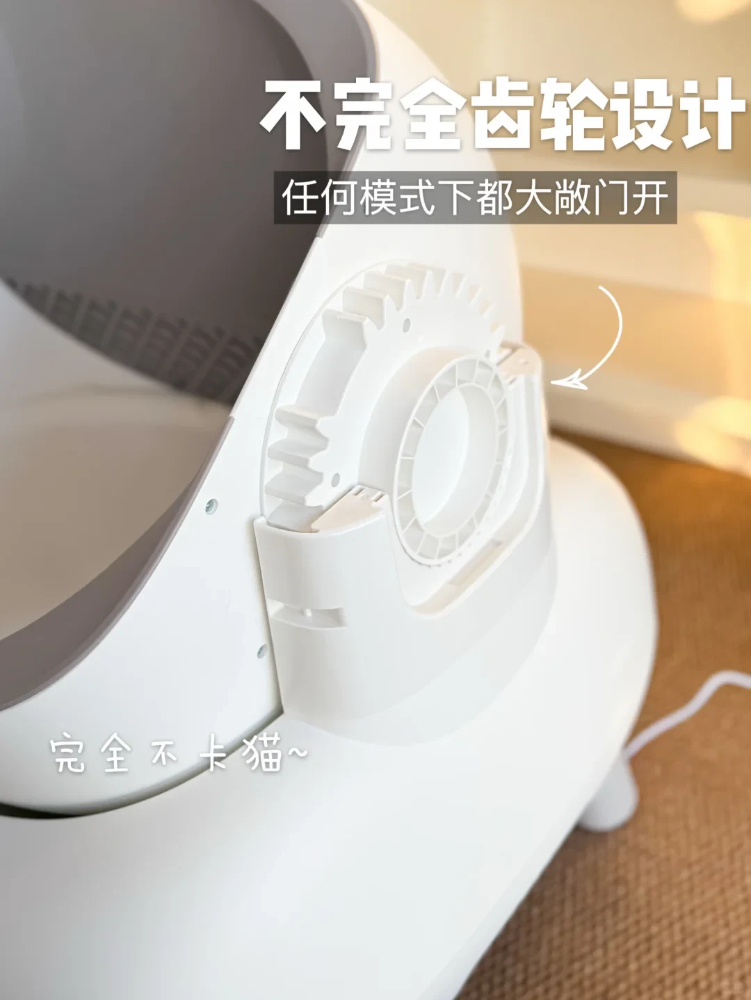 Close-up view of the side mechanism of a white automatic cat litter box, highlighting an incomplete gear structure with an open drum opening design.
