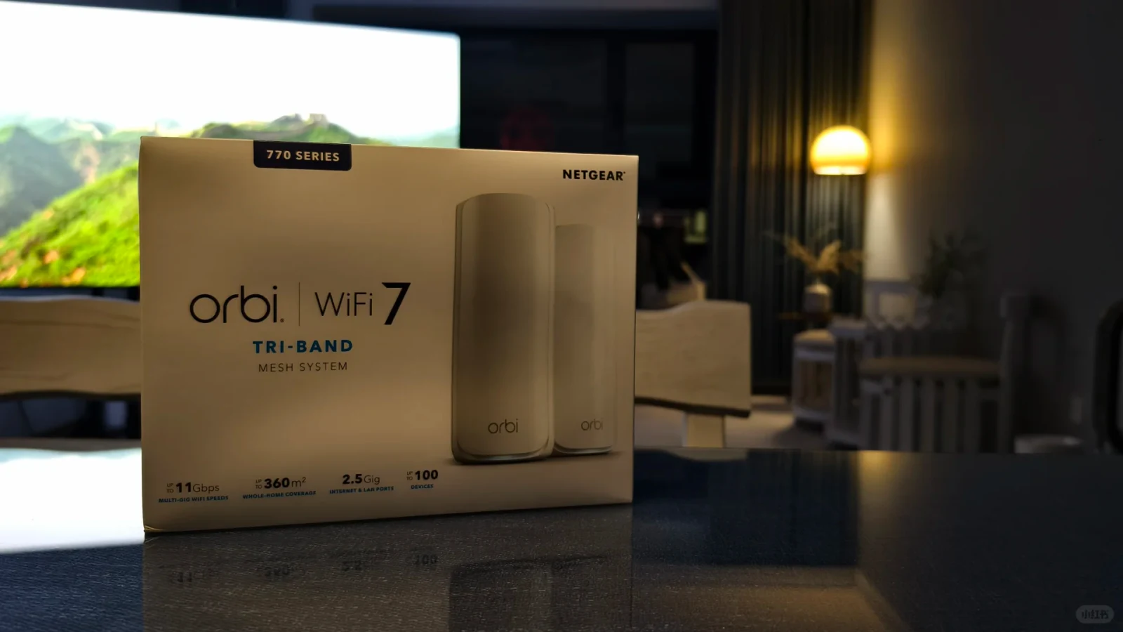 The retail packaging box for a Netgear Orbi 770 Series Tri-Band WiFi 7 mesh system sitting on a glossy table indoors.
