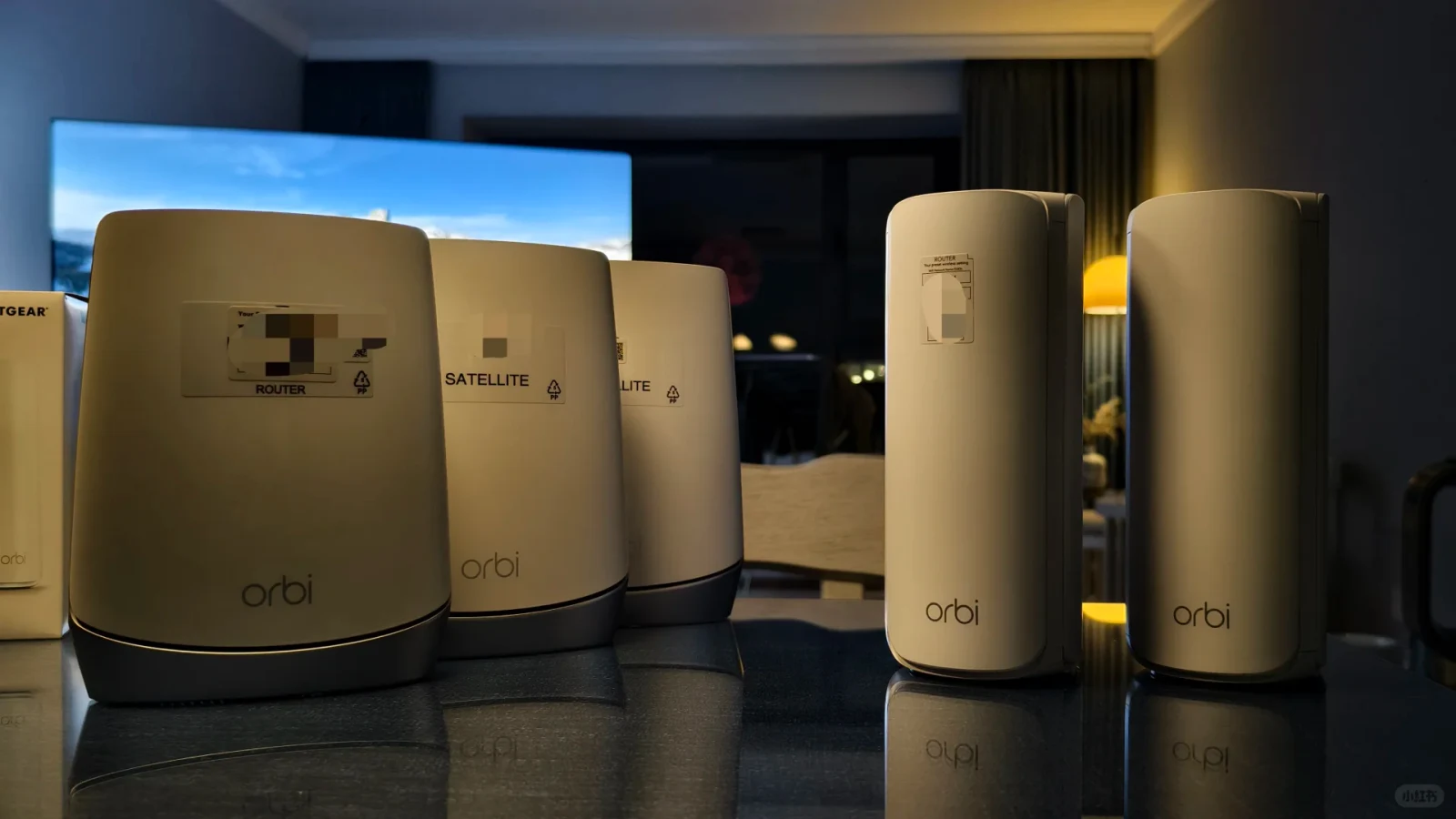 A row of white Netgear Orbi mesh Wi-Fi routers and satellites standing on a dark reflective tabletop in a living room.