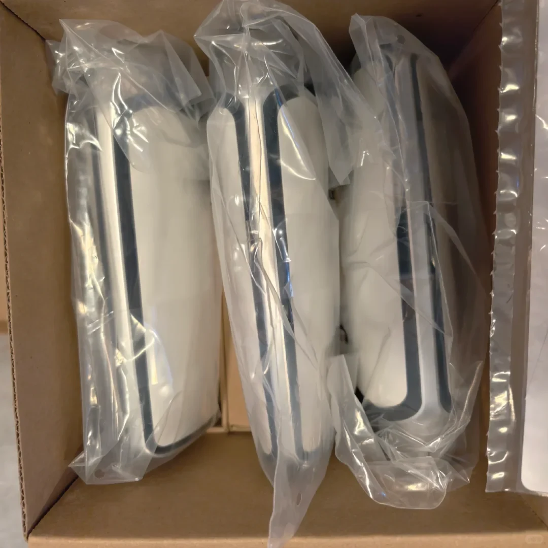 Three white and grey electronic accessories or covers individually packaged in clear plastic bags, packed upright inside a cardboard shipping box.